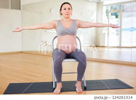 Pregnant woman is engaged in yoga. Exercise on chair with arms spread apart Pregnant woman is engaged in yoga. Exercise on chair with arms spread apart 124261314