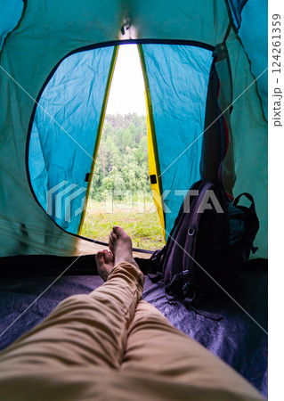 Relaxing within tent opening, green forest backdrop creating tranquil wilderness camping environment for outdoor retreat Relaxing within tent opening, green forest backdrop creating tranquil wilderness camping environment for outdoor retreat 124261359