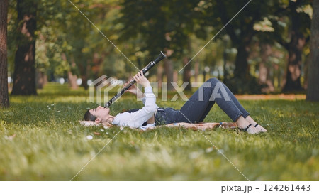 Young woman musician playing clarinet lying on grass in a park, enjoying music and nature Young woman musician playing clarinet lying on grass in a park, enjoying music and nature 124261443