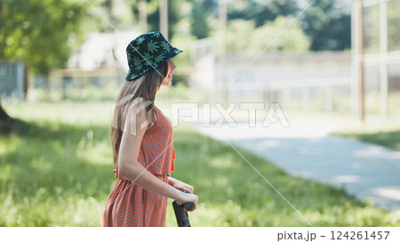 Woman riding electric scooter through verdant park, basking in warm summer sunlight and embracing leisurely outdoor moment Woman riding electric scooter through verdant park, basking in warm summer sunlight and embracing leisurely outdoor moment 124261457