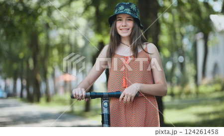 Happy teenager riding electric scooter in a summer park, enjoying sustainable transportation and outdoor activity Happy teenager riding electric scooter in a summer park, enjoying sustainable transportation and outdoor activity 124261458