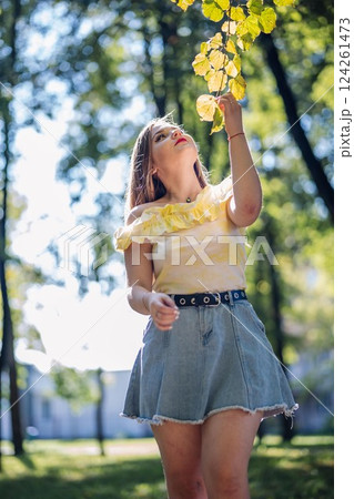 Young woman caressing vibrant autumn foliage, sunlight filtering through park trees, experiencing seasonal beauty 124261473