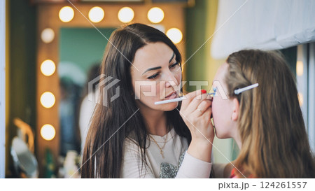 Professional makeup artist brushing vivid blue eyeshadow onto female model's eyelid in modern beauty studio 124261557