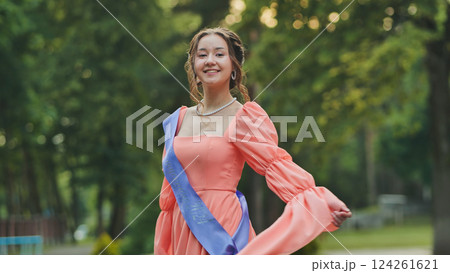 Young graduate wearing a vibrant graduation sash, joyfully celebrating the end of school while surrounded by lush greenery in a park Young graduate wearing a vibrant graduation sash, joyfully celebrating the end of school while surrounded by lush greenery in a park 124261621