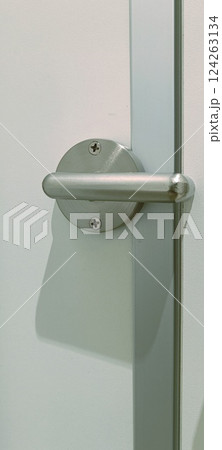A modern door handle is showcased with a polished surface and minimalist design. The handle is attached to a simple white door, emphasizing functionality and style. 124263134