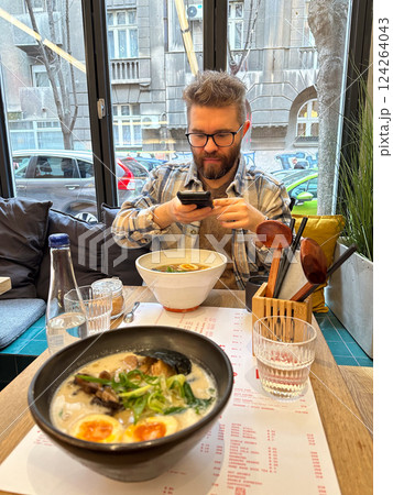 Man taking photo on smartphone while eating ramen soup. Japanese cuisine Man taking photo on smartphone while eating ramen soup. Japanese cuisine 124264043