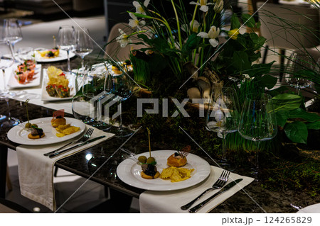 Luxurious dining table setup featuring gourmet appetizers, elegant glassware, floral centerpiece 124265829