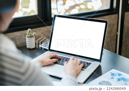 Hands typing on a laptop with a blank screen, placed on a desk by a window, featuring a small cactus and documents. 124266049