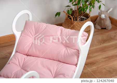 White wooden rocking bed adorned with pink cushions in a cozy indoor setting. Kids rocking bed placed in a warmly lit corner of a room with natural flooring and indoor decor White wooden rocking bed adorned with pink cushions in a cozy indoor setting. Kids rocking bed placed in a warmly lit corner of a room with natural flooring and indoor decor 124267040