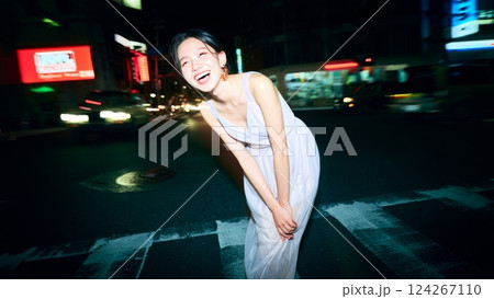 A flash-lit shot of a young woman wearing an elegant dress, in the middle of a busy city at night. Youth and happiness concept A flash-lit shot of a young woman wearing an elegant dress, in the middle of a busy city at night. Youth and happiness concept 124267110