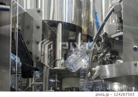 The empty drinking water bottles hanging on the conveyor belt for filling process. The empty drinking water bottles hanging on the conveyor belt for filling process. 124267503