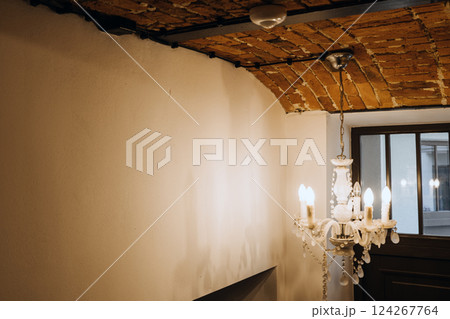 Interior with exposed electrical wiring on arched brick ceiling and vintage chandelier, blending rustic design with modern infrastructure. Visible wiring, interior design contrast, adaptive reuse. Interior with exposed electrical wiring on arched brick ceiling and vintage chandelier, blending rustic design with modern infrastructure. Visible wiring, interior design contrast, adaptive reuse. 124267764