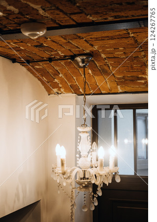 Interior with exposed electrical wiring on arched brick ceiling and vintage chandelier, blending rustic design with modern infrastructure. Visible wiring, interior design contrast, adaptive reuse. Interior with exposed electrical wiring on arched brick ceiling and vintage chandelier, blending rustic design with modern infrastructure. Visible wiring, interior design contrast, adaptive reuse. 124267765