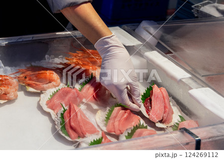 Vendor in gloves arranges fresh otoro fatty tuna sashimi on shiso leaves inside scallop shells 124269112