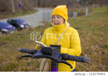 Woman in Yellow Jacket Renting Electric Scooter via App in Urban Park 124270943