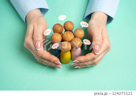 Hands in a protective gesture hold a group of human figures. Gather like-minded people together. Coordinate the team. 124271121