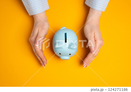 The piggy bank is protected by the hands of a woman in a protective gesture. Safeguarding personal savings, ensuring financial stability, and protecting assets. 124271186