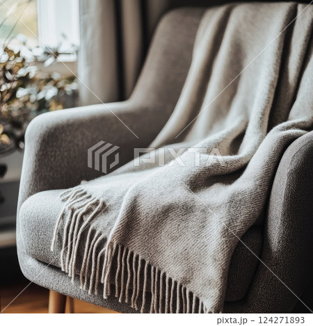 A cozy throw blanket mockup draped over the arm of a chair, with a soft-focus background in muted colors, creating a relaxing and welcoming ambiance for a peaceful space. 124271893