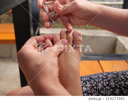 Mother carefully trimming her kid's toenails using a nail clipper, ensuring hygiene and foot health 124271981