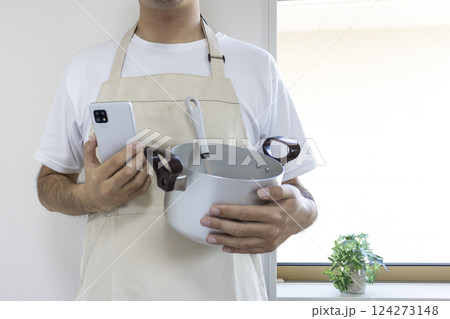 鍋とスマートフォンを持ちエプロンを付けた男性（顔無し、日本人、30代） 124273148