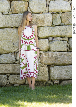 Young woman wearing summer dress leaning against stone wall 124273258