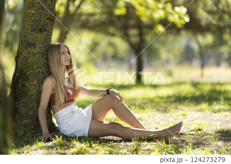 Young woman relaxing leaning on a tree in a park Young woman relaxing leaning on a tree in a park 124273279