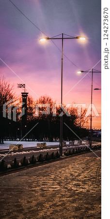Fantastic winter landscape at fiery dawn. Silhouette of lighthouse and walking paths in park 300 anniversary of St. Petersburg, Russia. Vertical photo. 124273670