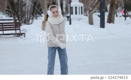 Teenage girl gliding confidently across icy rink, wearing warm winter outfit. Bright smile expressing pure happiness during seasonal outdoor skating experience 124274013