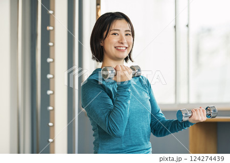 スポーツジムで鉄アレイを使って筋トレをする女性 124274439