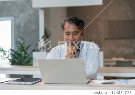 Focused Engagement and Digital Consulting. A senior man attentively reviews business information on his laptop. 124274777