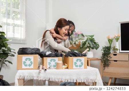 Family Connection and Recycling Efforts. A joyful mother and daughter embrace while sorting out recyclable items in an eco-friendly manner. Family Connection and Recycling Efforts. A joyful mother and daughter embrace while sorting out recyclable items in an eco-friendly manner. 124274833