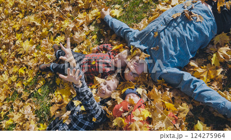 Smiling family resting on colorful fallen leaves, basking in warm sunlight, sharing laughter amid autumn's golden landscape Smiling family resting on colorful fallen leaves, basking in warm sunlight, sharing laughter amid autumn's golden landscape 124275964