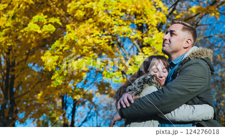 Loving couple embracing beneath golden hued trees, sharing intimate moment amid autumn sunlight in peaceful park landscape Loving couple embracing beneath golden hued trees, sharing intimate moment amid autumn sunlight in peaceful park landscape 124276018