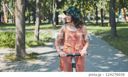 Young woman riding electric scooter through park, experiencing urban eco friendly transportation under bright sunlight 124276036
