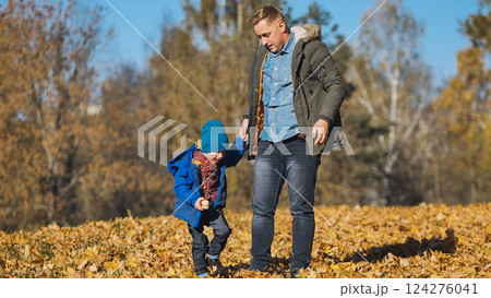 Father walking with son through park, sharing moment amid golden autumn foliage and scattered crisp leaves 124276041