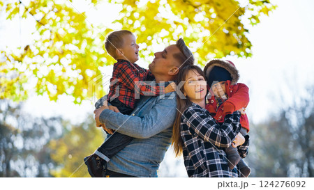 Parents holding their two sons, enjoying a sunny autumn day in a park, surrounded by colorful fall foliage Parents holding their two sons, enjoying a sunny autumn day in a park, surrounded by colorful fall foliage 124276092
