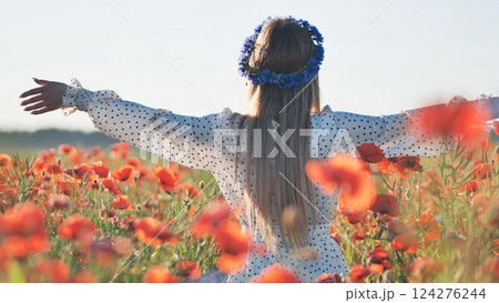 Young blonde woman with open arms, wearing a blue flower crown, enjoying freedom in a red poppy field Young blonde woman with open arms, wearing a blue flower crown, enjoying freedom in a red poppy field 124276244