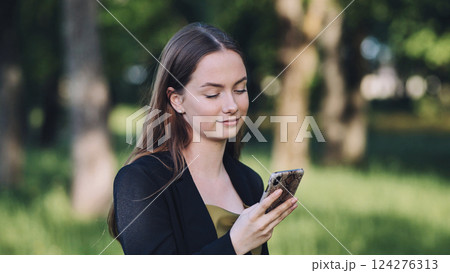 Smiling businesswoman using mobile phone in a park, enjoying online activity during break 124276313