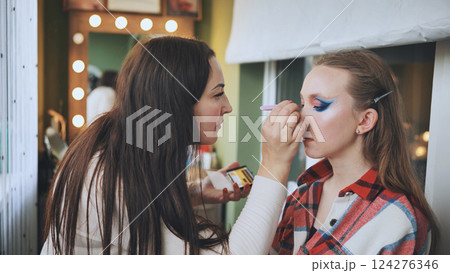 Makeup artist blending vivid eyeshadow on model's eyelids, highlighting professional beauty technique in salon environment Makeup artist blending vivid eyeshadow on model's eyelids, highlighting professional beauty technique in salon environment 124276346