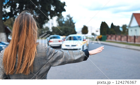 Professional woman gesturing for taxi while standing on crowded downtown sidewalk, capturing city's dynamic work environment 124276367