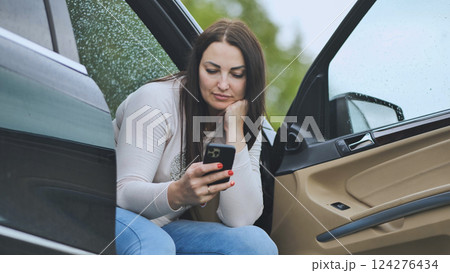 Businesswoman using smartphone while sitting in her car with open door, checking messages or browsing social media 124276434