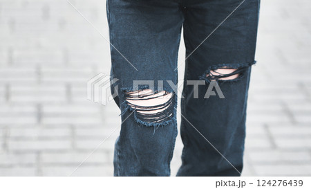Close up of ripped black jeans on a girl walking on a paved street, showcasing urban style and fashion trends Close up of ripped black jeans on a girl walking on a paved street, showcasing urban style and fashion trends 124276439