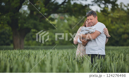 Cheerful family bonding outdoors, cuddling newborn among lush grass and wildflowers Cheerful family bonding outdoors, cuddling newborn among lush grass and wildflowers 124276498