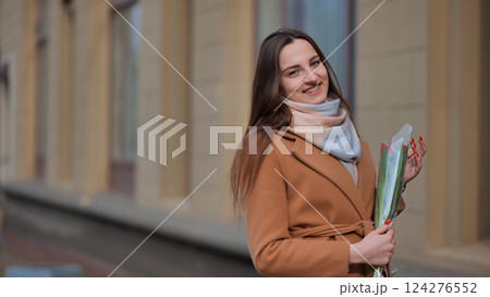 Portrait of a happy brunette girl with a tulip in the background of the city in the cold season. 124276552