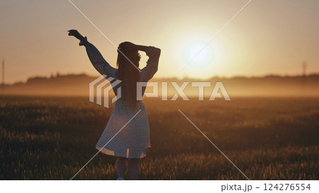 Slavic woman wearing white dress enjoying freedom in nature at sunset, walking in field with arms raised Slavic woman wearing white dress enjoying freedom in nature at sunset, walking in field with arms raised 124276554