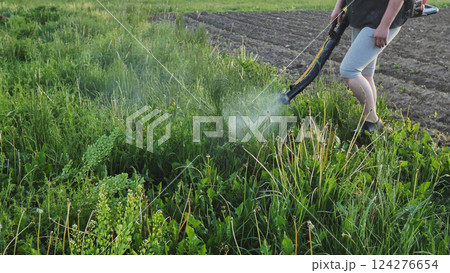 Farmer spraying pesticides with backpack sprayer near plowed field rows, targeting weeds Farmer spraying pesticides with backpack sprayer near plowed field rows, targeting weeds 124276654