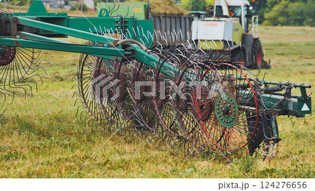 Green rotary hay rake turning grass in the field during summer harvest season, preparing hay for baling 124276656
