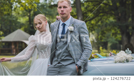 Newlyweds smiling, embracing near vintage car with wedding decor, green park backdrop highlighting romantic celebration moment Newlyweds smiling, embracing near vintage car with wedding decor, green park backdrop highlighting romantic celebration moment 124276722