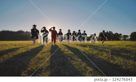 Group of cheerful graduates running together in a field at sunset, celebrating the end of high school Group of cheerful graduates running together in a field at sunset, celebrating the end of high school 124276843