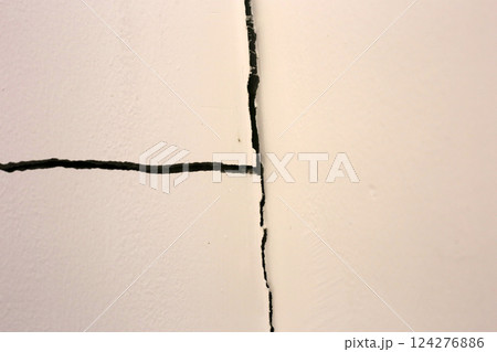 Close-up of a large crack running vertically and horizontally across an interior wall. 124276886